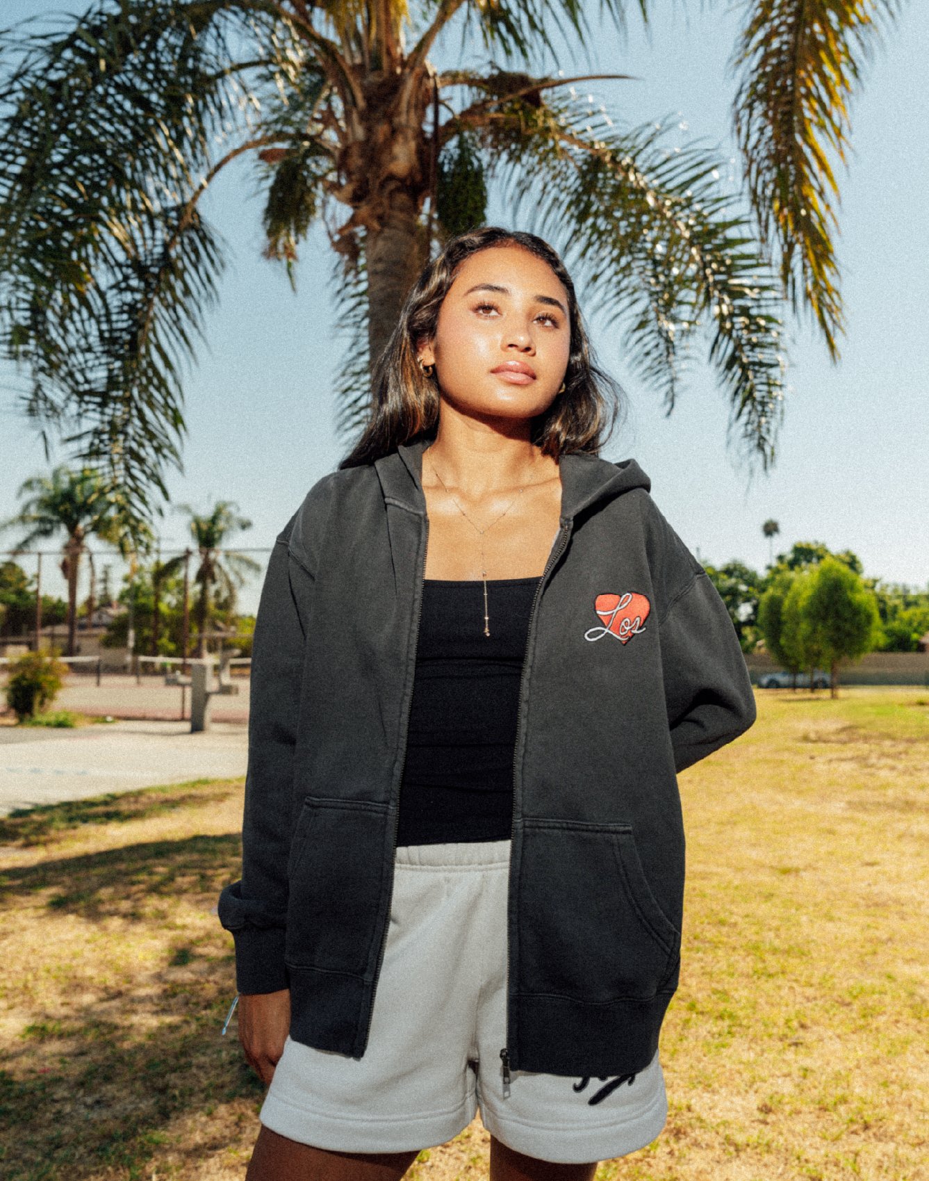 Alyssa Thompson posing in a Lockeroom's Los Angeles Zip Hoodie in front of palm tree.